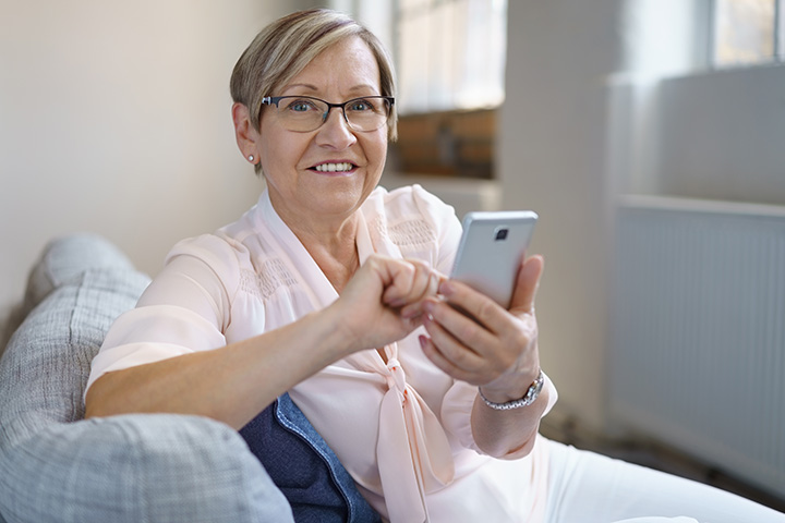 Portrait,Of,Cheerful,Senior,Woman,Using,Smartphone,While,Sitting,On